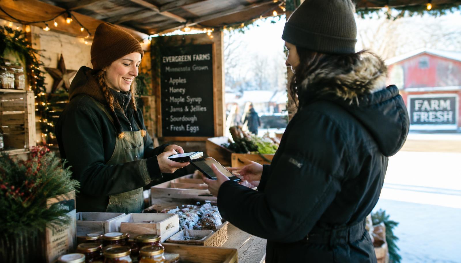 Seasonal outdoor market vendor accepting a card payment with a mobile card reader at a Minnesota holiday market